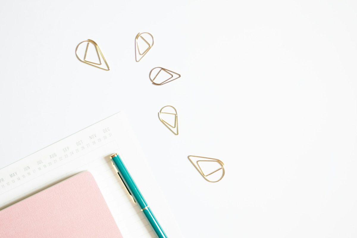 Notebook, pen, loose paper and paper clips on a white desk
