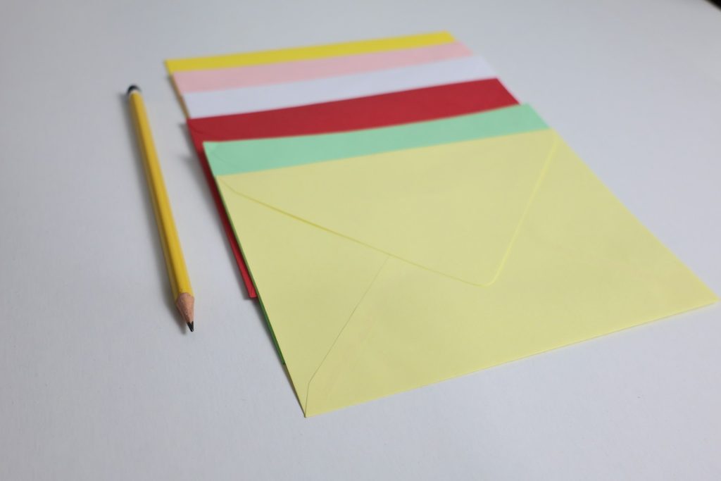 Colored envelopes arranged beside a yellow pencil on a white surface