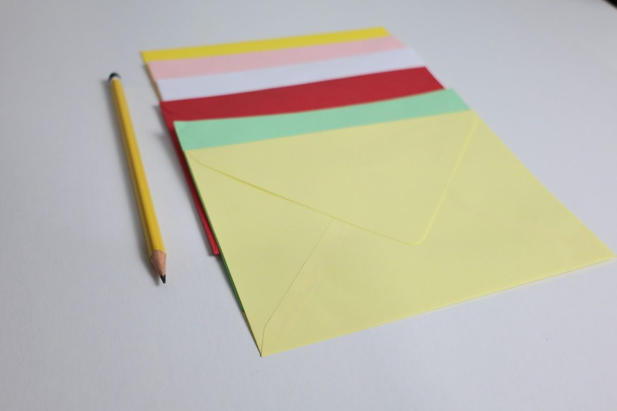 Colored envelopes arranged beside a yellow pencil on a white surface